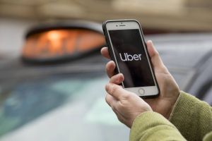 A commuter uses the Uber Technologies Inc. app on a smartphone in view of a black cab waiting to pick up passengers in this arranged photograph in London on Nov. 25, 2019. Foto: Bloomberg photo by Jason Alden