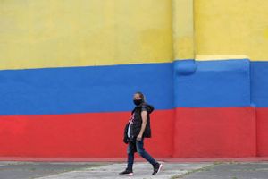 A woman wearing a protective face mask walks next to a house painted with colors of Colombia's flag, during the lockdown ordered by the government in an effort to prevent the spread of the new coronavirus, in Bogota, Colombia, Tuesday, April 14, 2020. Foto: AP Photo/Fernando Vergara