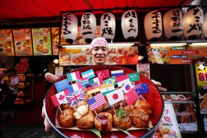 En sælger i Osaka præsenterer et fad med takoyaki forsynet med G20-landenes flag som symbol på, at havnebyen er ved at være parat til at tage imod de tusinder af deltagere i topmødet for stats- og regeringscheferne på fredag og lørdag. Takoyaki er stykker af blæksprutte arm i en dejkugle, der steges i noget, der mest af alt minder om en æbleskivepande. Foto: AP
