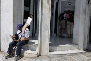 Et par turister hæver penge ved en græsk pengeautomat i juni 2015 i Athen i Grækenland. Foran sidder en mand og sælger Lottokuponer